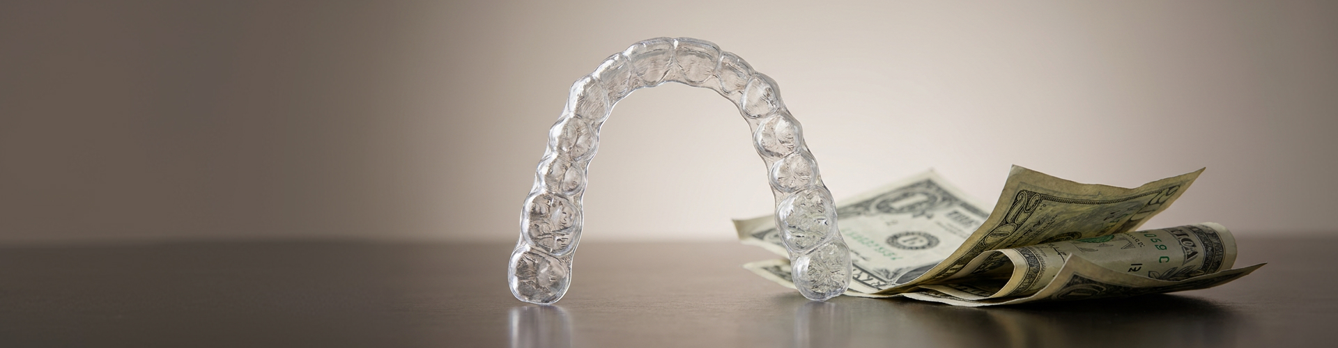 Clear aligner beside dollar bills.